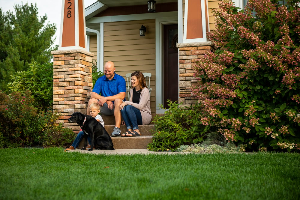 family sits on porch with dog in front of green lawn