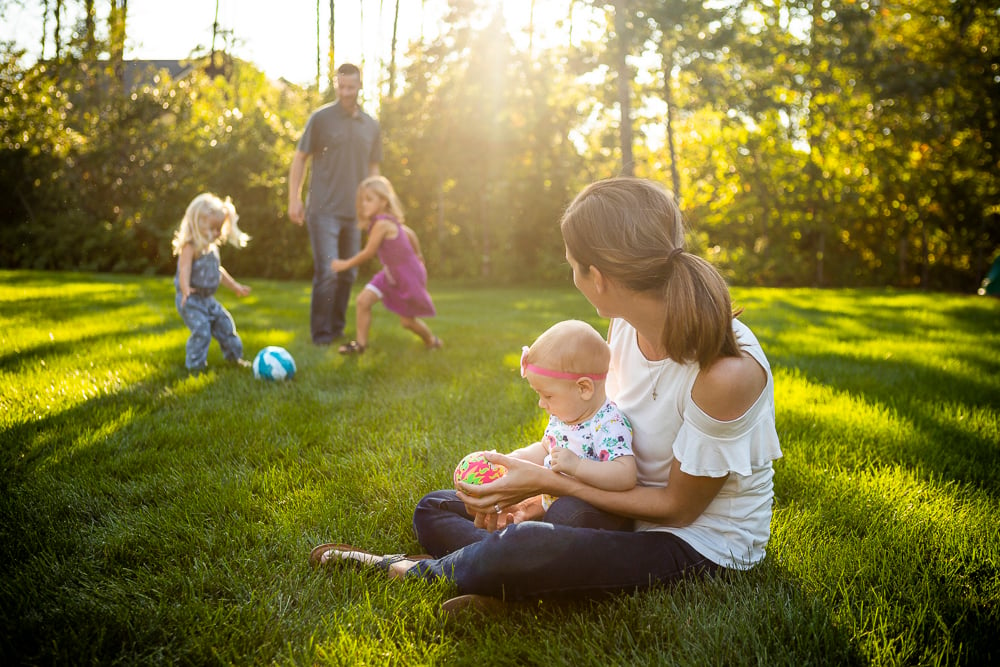 family sits in grass playing with soccer ball