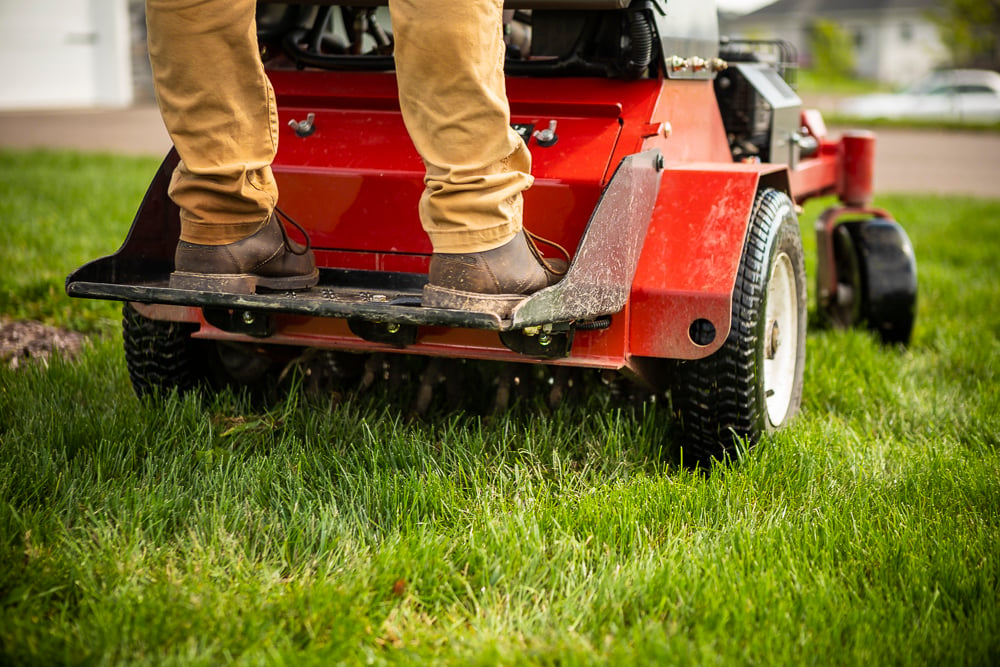 lawn care technician operating powered aerator on lawn