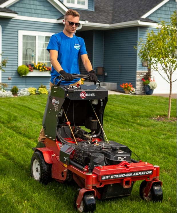 lawn care technician operating a stand-on aerator in a nice lawn