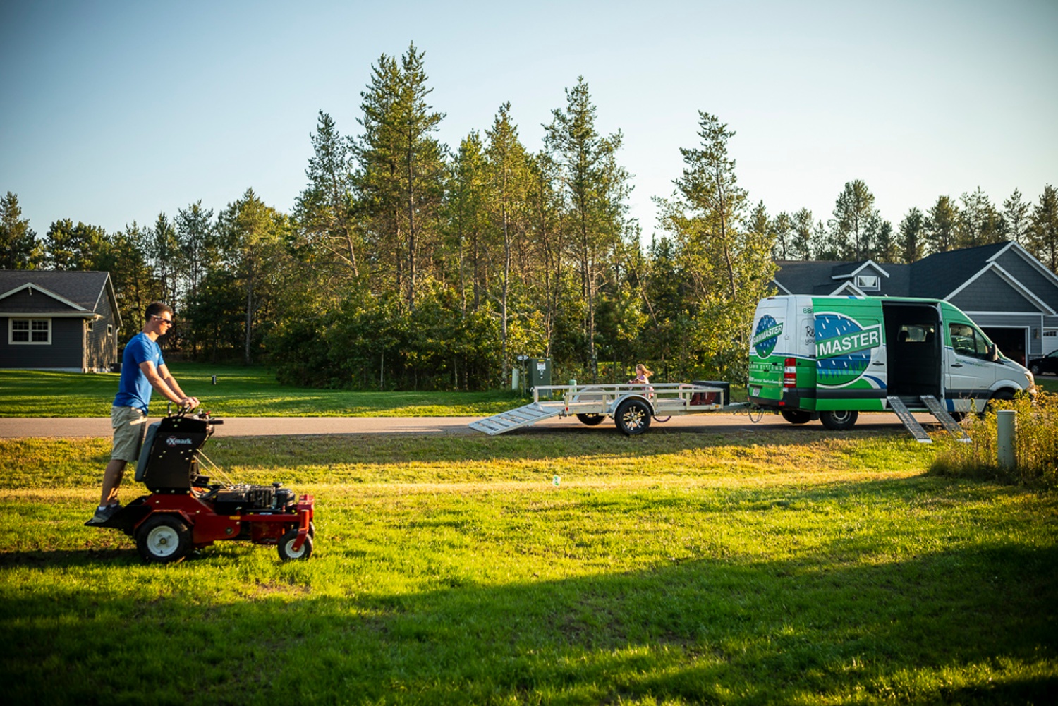 lawn care technician aerating a lawn with landscaping company truck in background