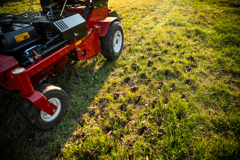 lawn care technician operating powered aeration machine in lawn