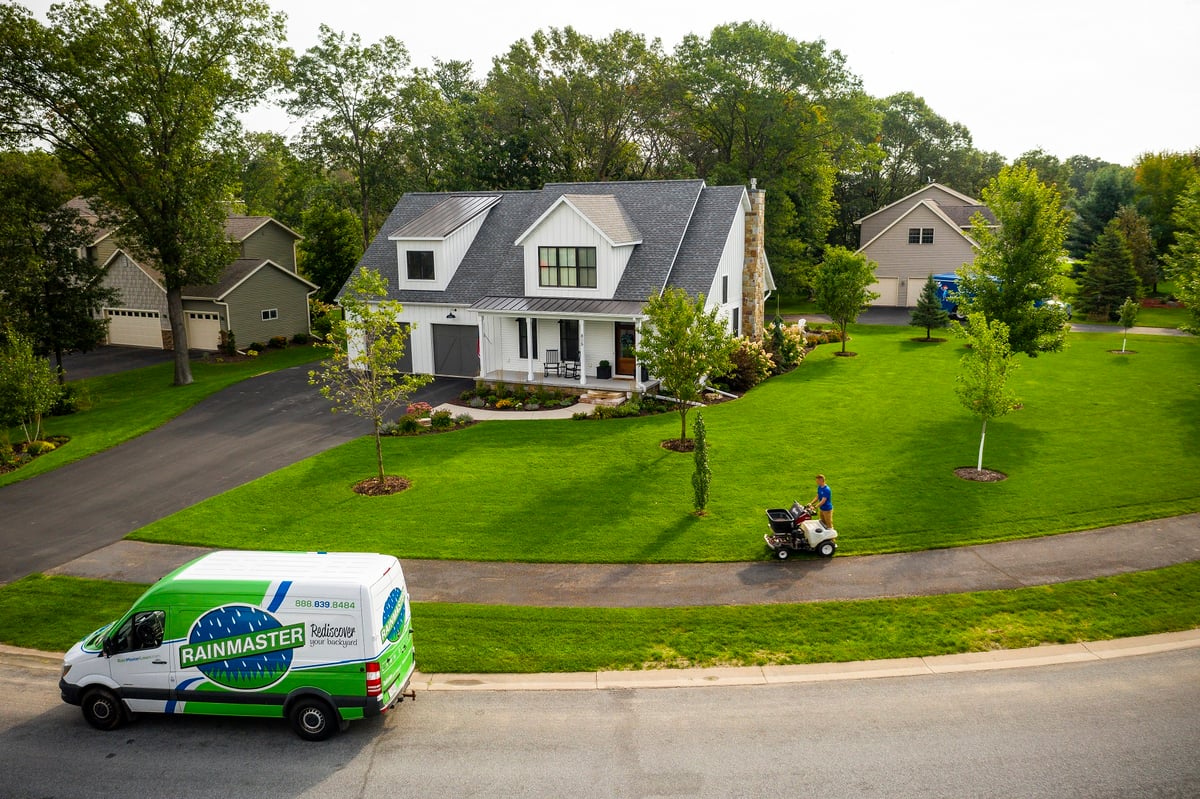 aerial photo of home with lawn care technician fertilizing lawn