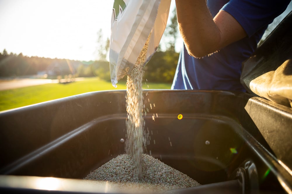 lawn team member pours fertilizer into spreader