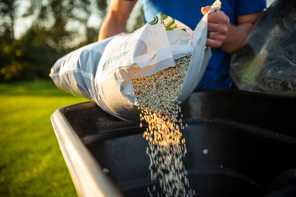 lawn team pours fertilizer into spreader