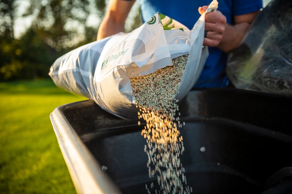 granular fertilizer being poured into spreader