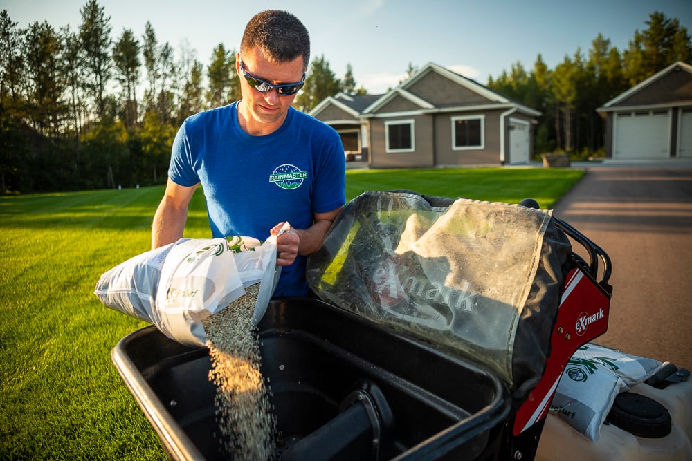lawn team pours granular fertilizer into spreader