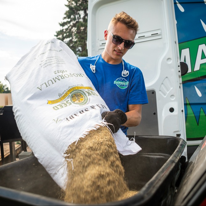 lawn care technician filling a lawn spreader with grass seed