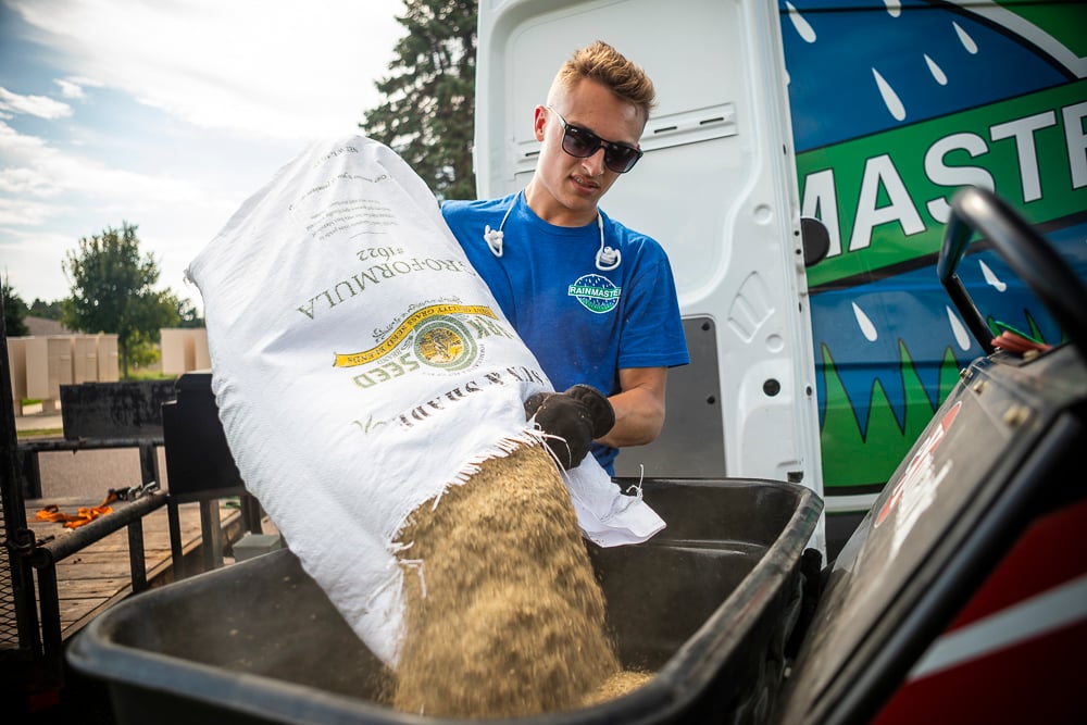 lawn team pours grass seed into spreader