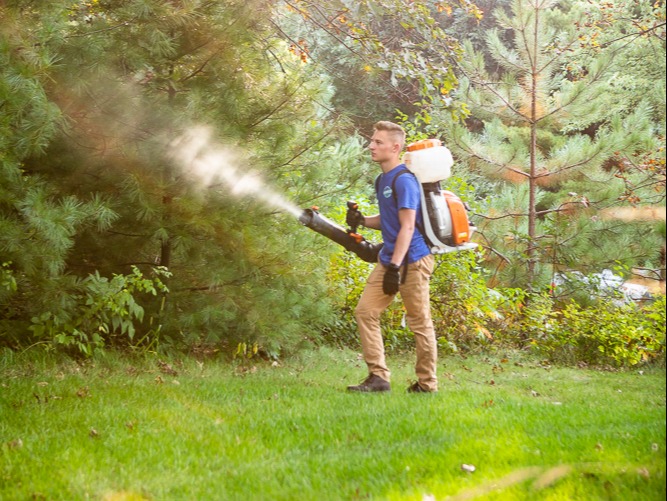 pest control technician applying mosquito barrier spray to woodline