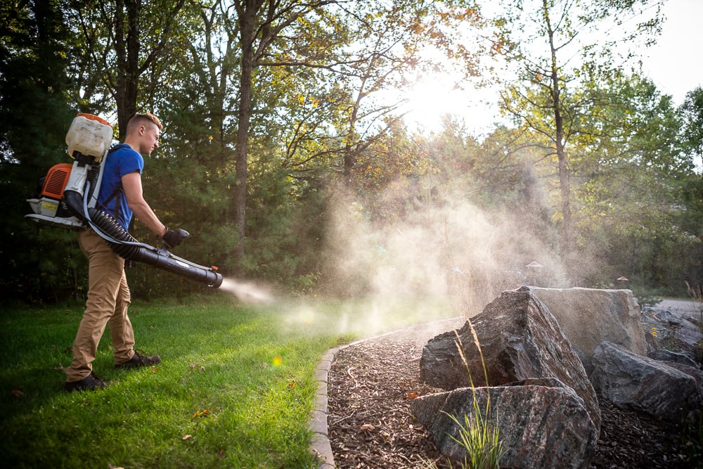 pest control technician sprays landscape bed for mosquitoes and ticks
