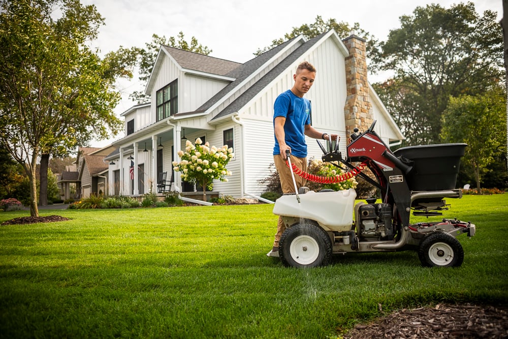lawn care technician spot-spraying lawn weeds with fertilization machine