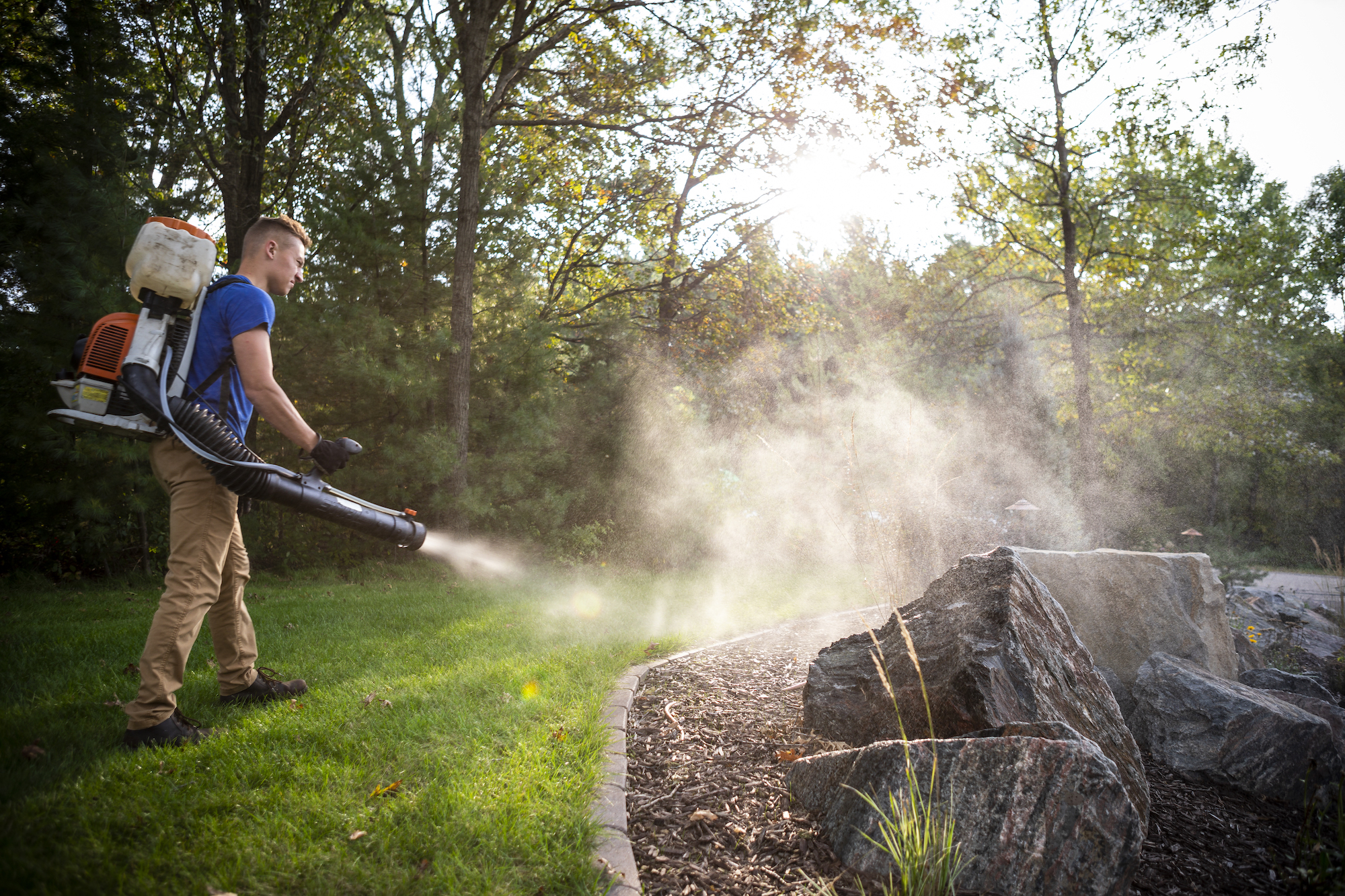 pest control technician spraying mosquito barrier spray to edge of landscape bed