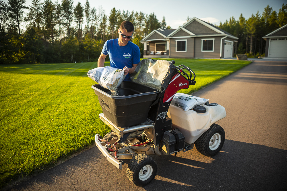lawn care professional pours fertilizer into spreader