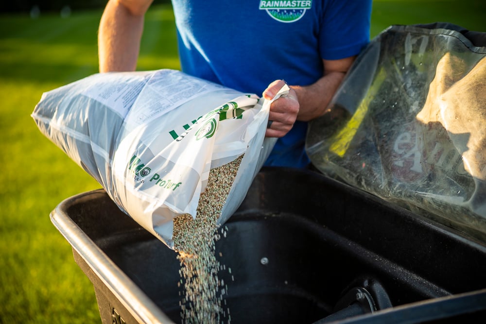 lawn care technician filling a spreader with granular fertilizer