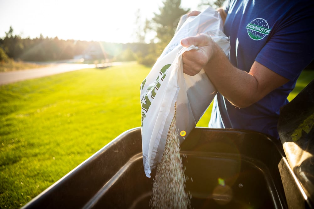 lawn care technician filling a spreader with granular fertilizer