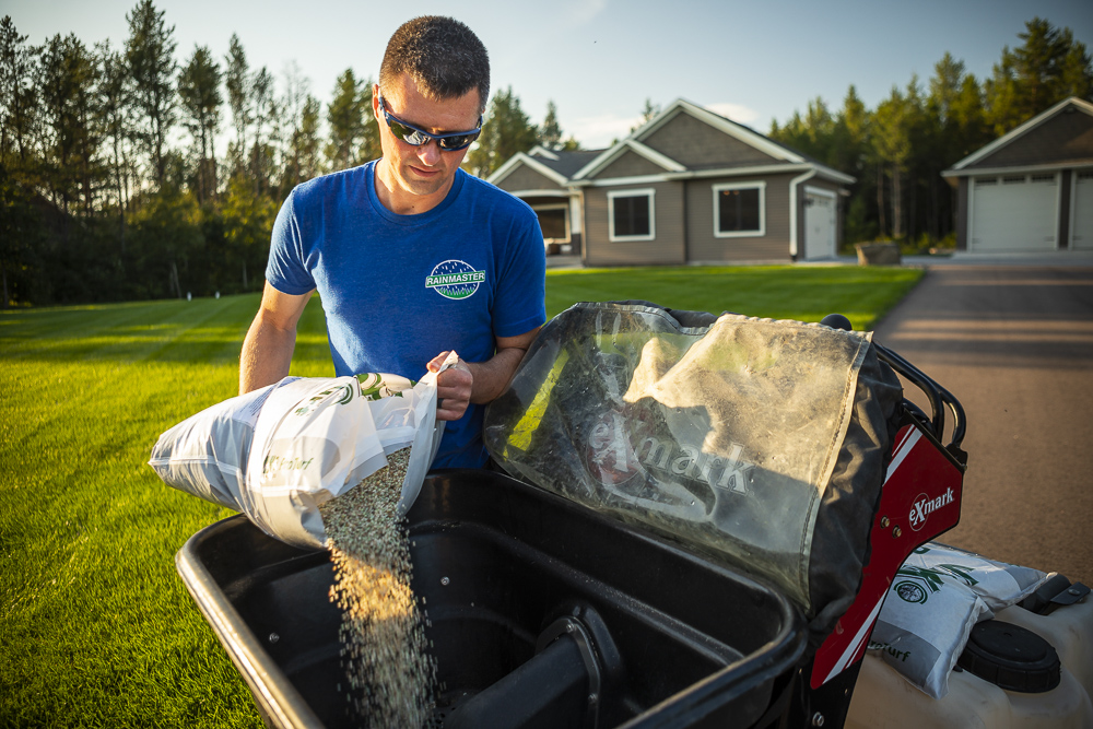 lawn technician pours fertilizer into spreader