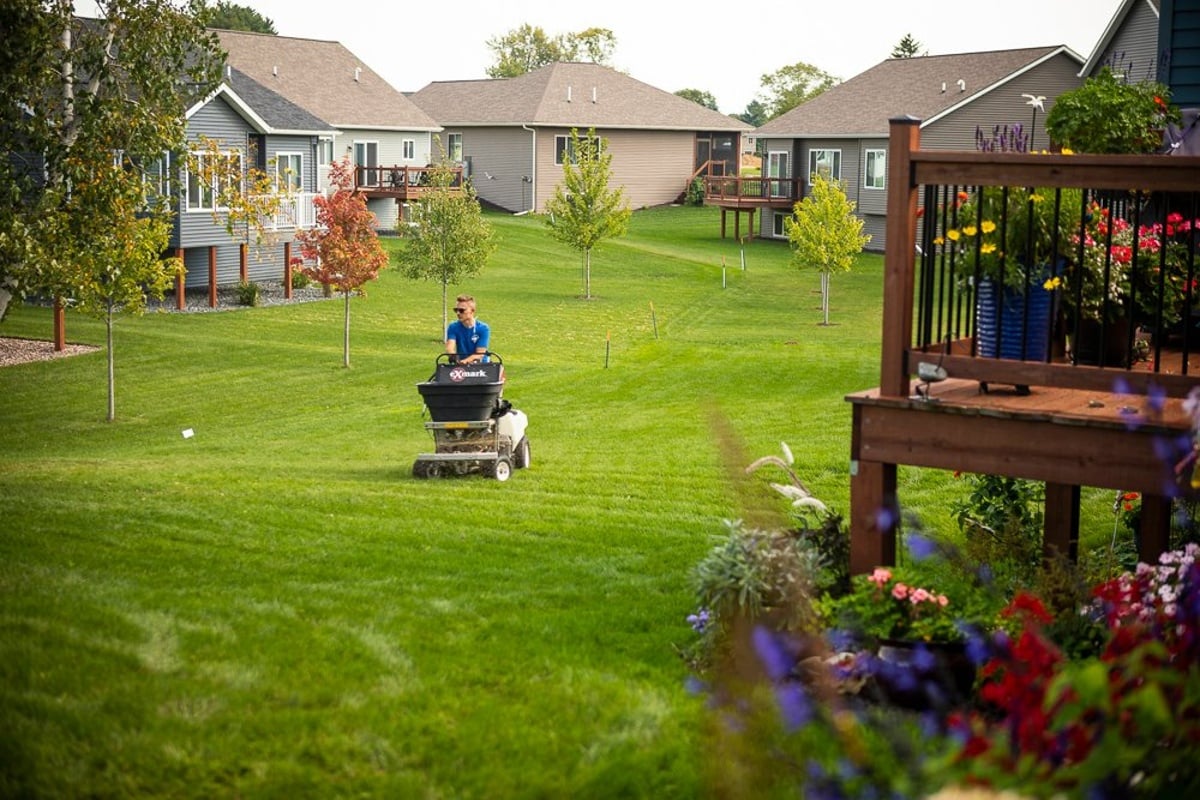 lawn care technician running a fertilizer spreader on an HOA lawn