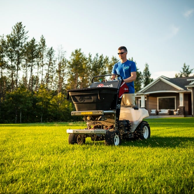 lawn care technician spreading granular fertilizer on a lawn