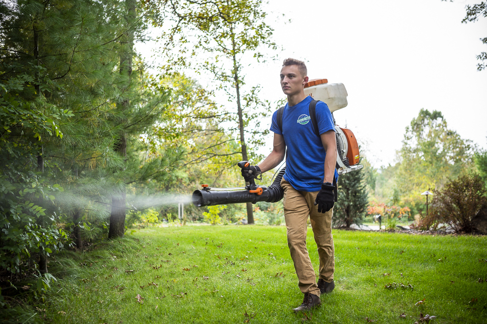 pest control technician sprays for mosquitoes and ticks